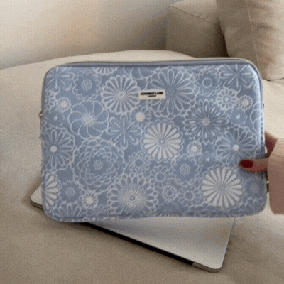 Baby blue floral laptop sleeve partially covering a silver laptop on a beige couch, hand nearby.