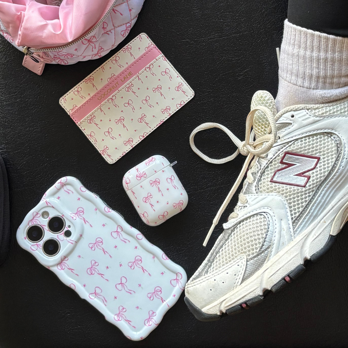 Card holder with pink bows on black, white sneaker with sock, vegan wallet, AirPods case, phone case with pink bows.