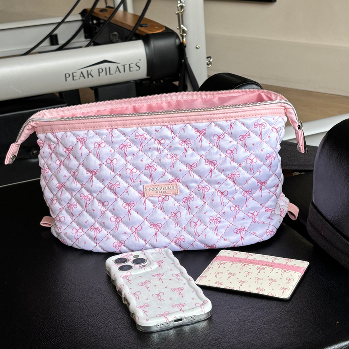 Pink and white quilted vegan leather card holder with bow detail resting on black Peak Pilates equipment.