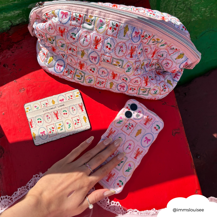 Manicured hand on pastel phone case, beside patterned Dolce Vita card holder and blue Mediterranean-style wallet.