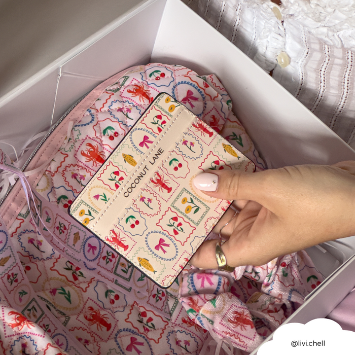 Hand holds a patterned Dolce Vita card holder by Coconut Lane above matching fabric inside an open box.