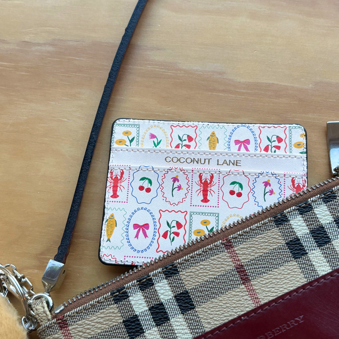 Dolce Vita card holder with gold lettering next to a plaid Burberry pouch on a wooden surface.