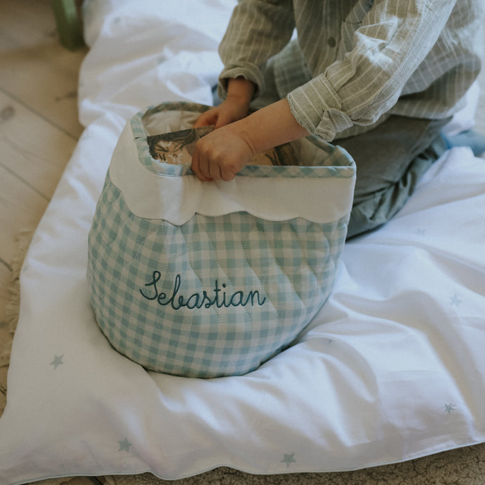 Person sitting on a baby duvet with a checkered laundry basket labeled 'Sebastian'.