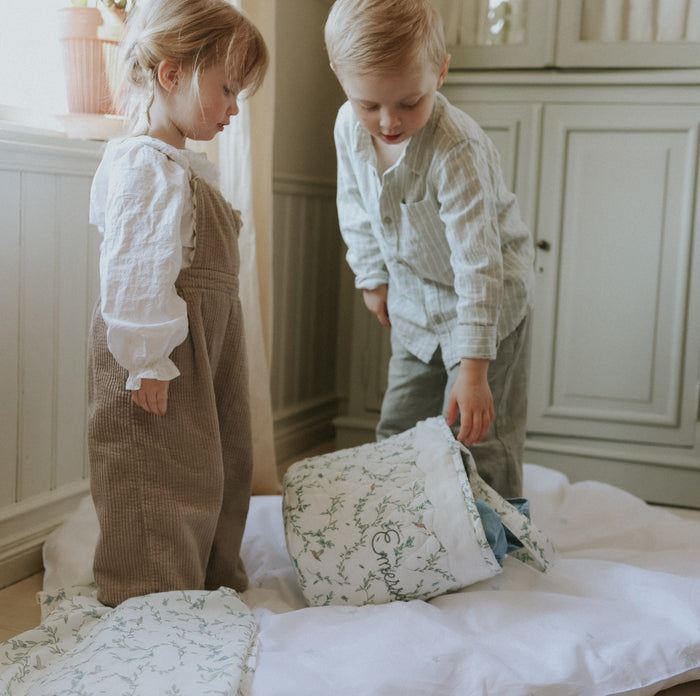 Two children playing with pillows on a bed in a bedroom.