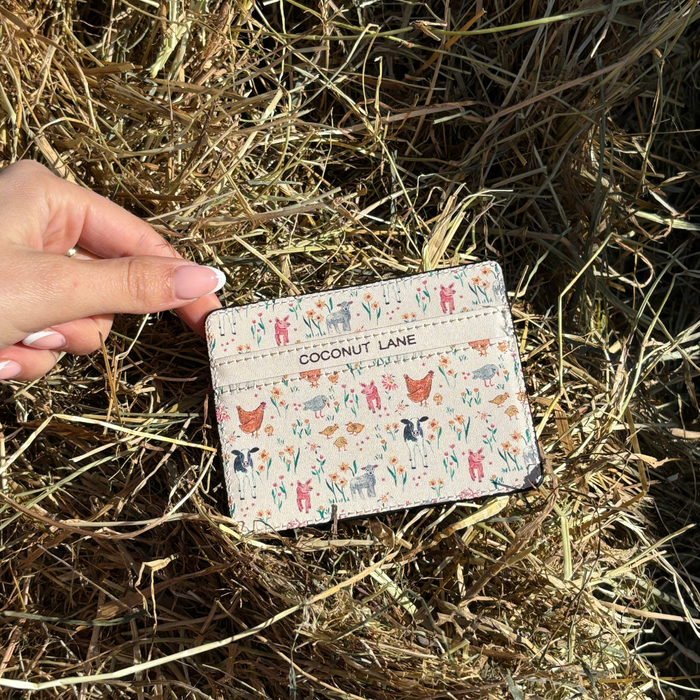 Hand holding Coconut Lane card holder with colorful animal prints, shown over dry grass in sunlight.