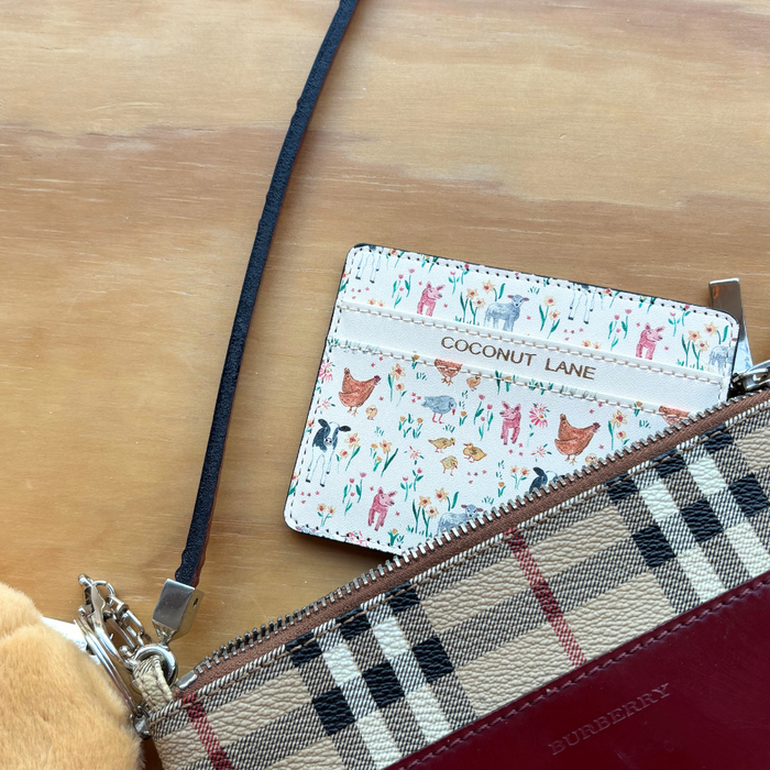 Farmyard Friends card holder partially tucked into a plaid Burberry pouch on a wooden surface.