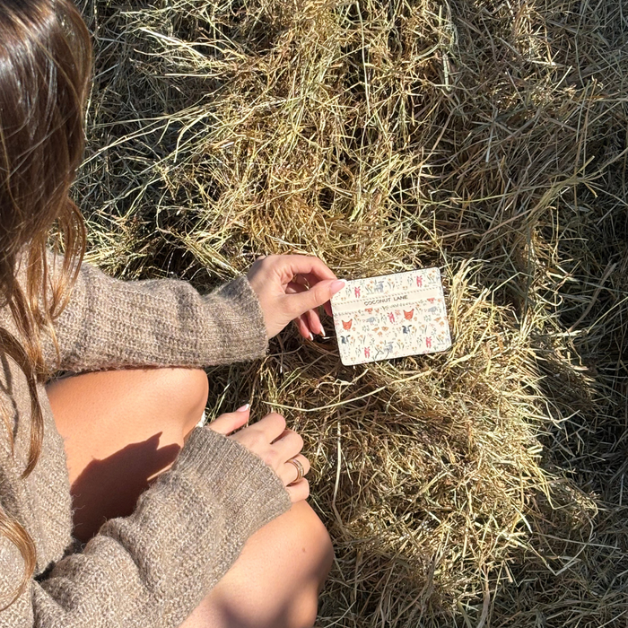 Person in brown sweater on hay holds a pastel Farmyard Friends card holder from Coconut Lane, shown in sunlight.