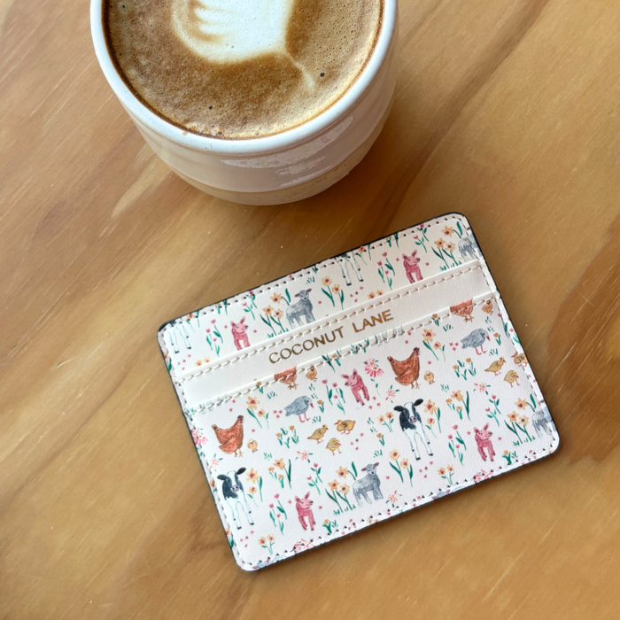 Coconut Lane Farmyard Friends card holder with colorful animal and flower design beside a cup of coffee.
