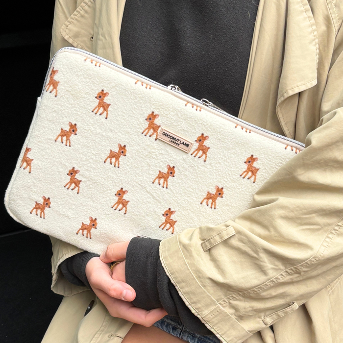 Beige-coated person holding a fleecy laptop sleeve with brown fawn print and a visible zipper.