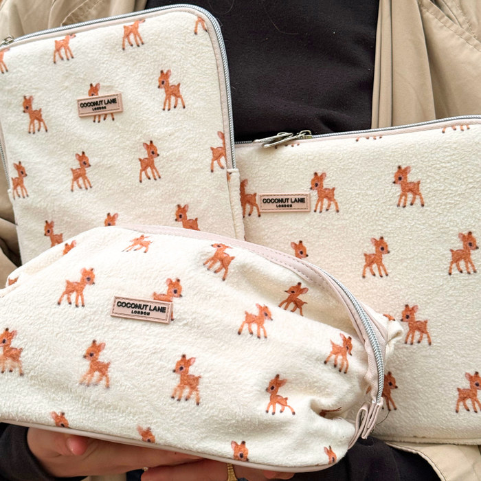 Three white laptop sleeves with brown deer print, labelled Fleecy Fawn by Coconut Lane, held in someones arms.