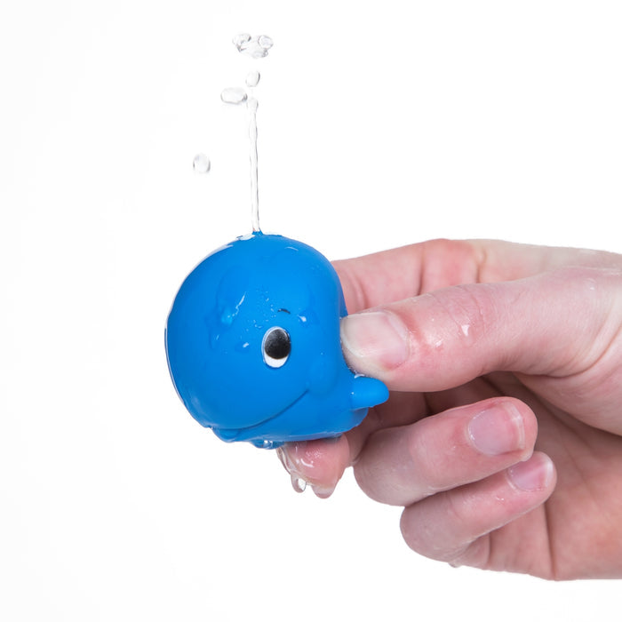 A hand squeezes a blue fish from the Nuby Fun Fish Squirters 3-pack, making water squirt from a top hole with a white background.