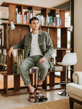 Man sitting on a stool in front of a wooden bookshelf in a modern living room.