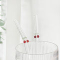 Two clear glass straws with red cherry accents in a ribbed glass cup.