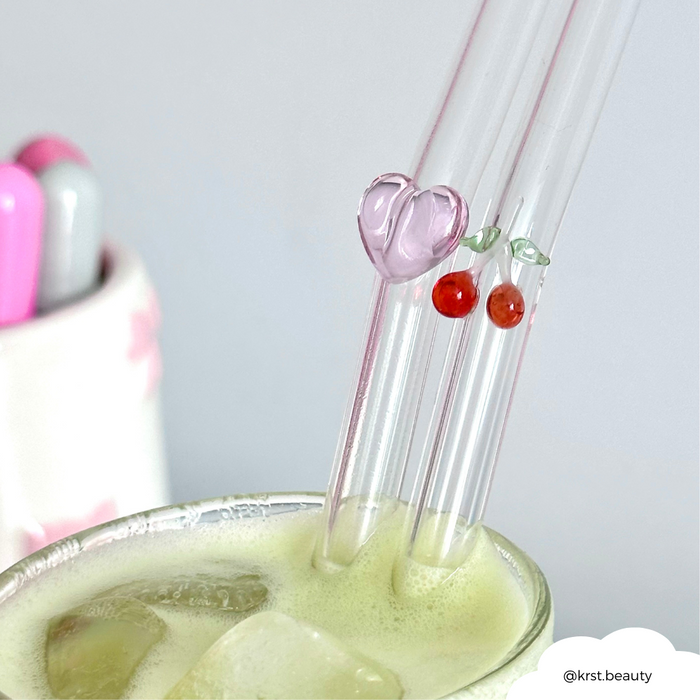 Two clear glass straws with heart and cherry patterns in an iced green drink.