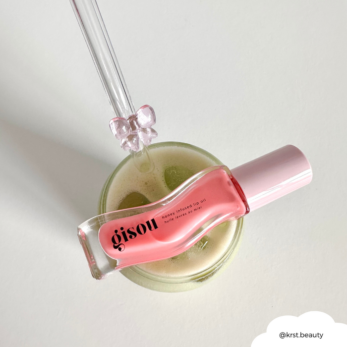 Pink Gisou lip oil on a green drink, with a pink bow-topped glass straw, set against a light background.