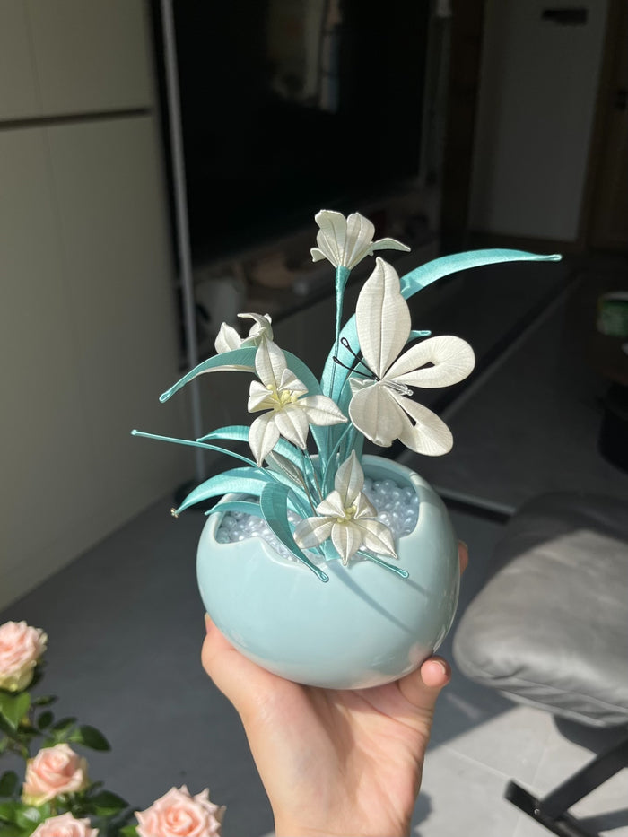 A black graduation cap adorned with white handmade Chanhua and turquoise - colored leaves, held by a hand-4