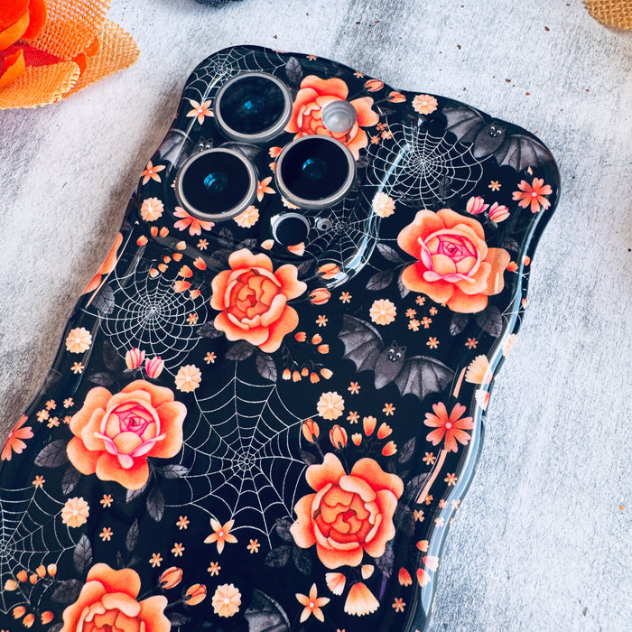 Close-up of the Haunted Blossoms Wavy Luxe MagSafe iPhone case on marble showing gold spiderwebs woven between coral roses.