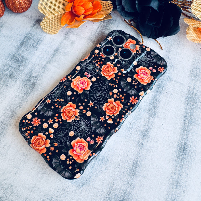 Haunted Blossoms Wavy Luxe MagSafe iPhone case laid flat on marble with an orange bloom and black tulle behind it.