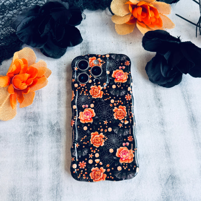 Haunted Blossoms Wavy Luxe MagSafe iPhone case shown flat on marble, displaying the full black and coral gothic floral print.