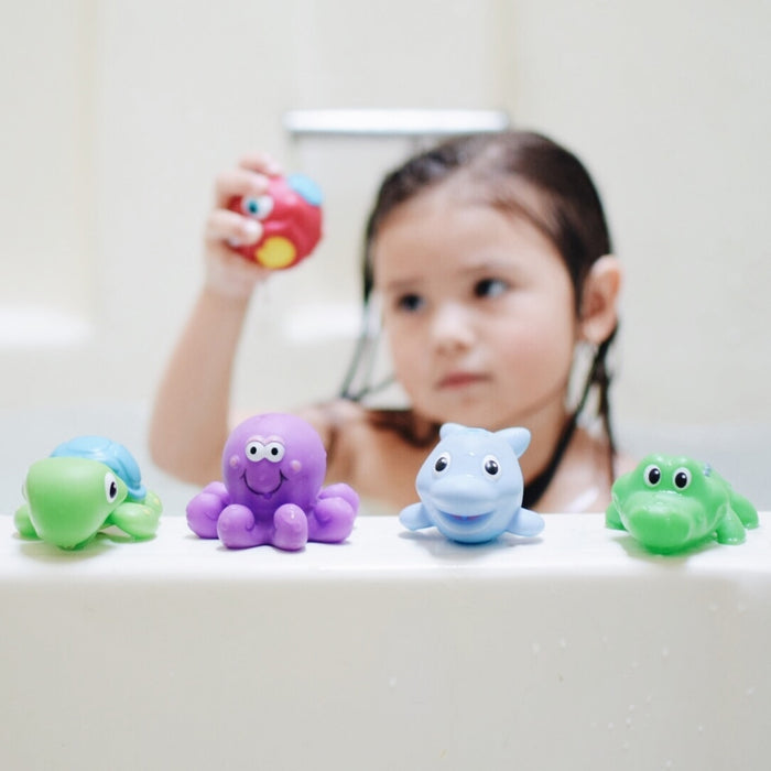 A young child in the tub holds a red toy, with four colorful Little Squirts Bath Squirters—turtle, octopus, dolphin, and alligator—lined up on the tub edge. These fun toys squirt water for extra bath time joy.