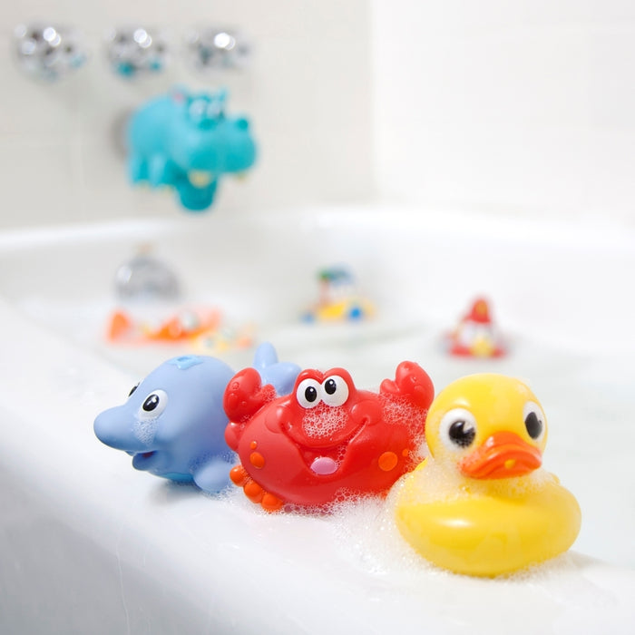 Three Little Squirts Bath Squirters—a blue dolphin, red crab, and yellow duck—sit on the bubbly tub’s edge, with a blue hippo faucet cover in the background.