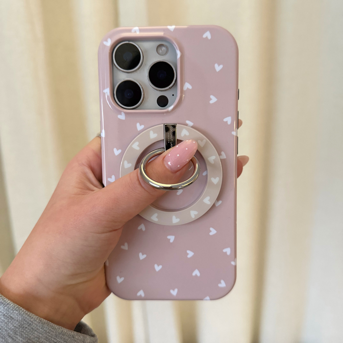 Pink-nailed hand holds a Coconut Lane chai hearts MAGSAFE® phone ring on a pink phone case with white hearts.