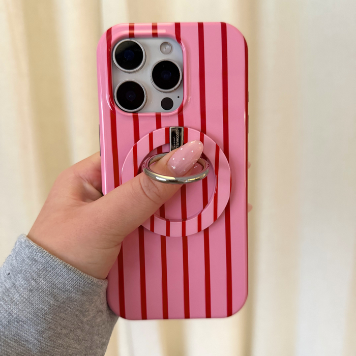 Hand holding a Coconut Lane MAGSAFE® Phone Ring with cherry stripes on a pink phone with red vertical stripes.