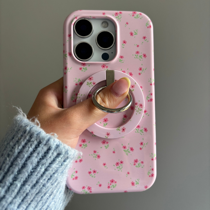 Hand holding a phone with a pink floral Coconut Lane MAGSAFE® Phone Ring, shown against a plain background.