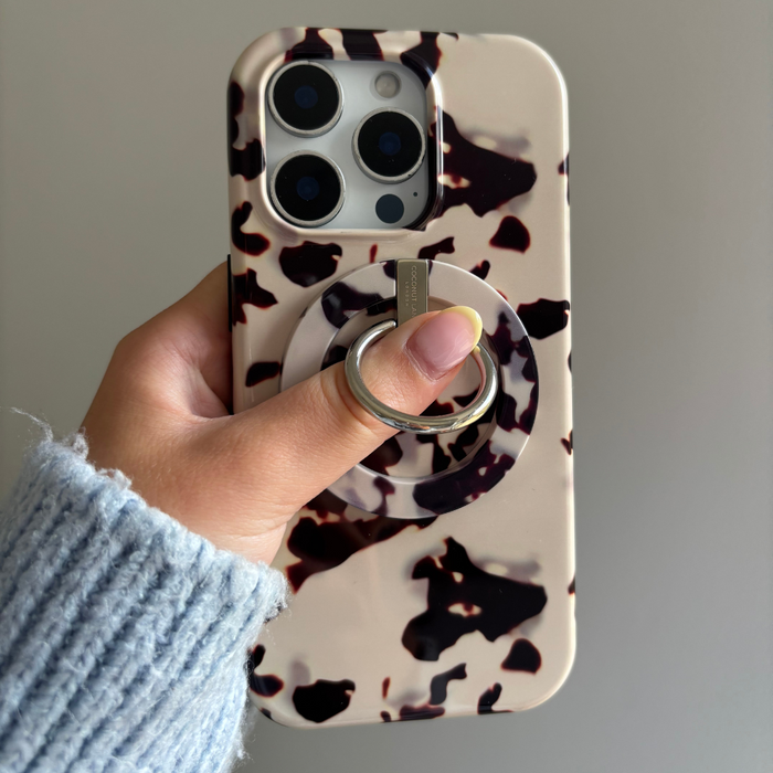 Hand holding phone with Ivory Tort Coconut Lane MAGSAFE® Phone Ring case, shown against a plain background.
