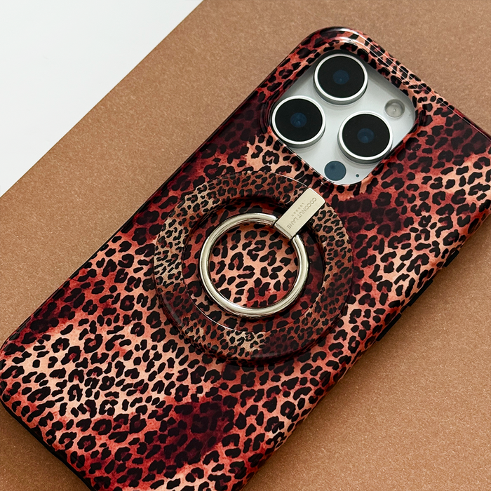 Smartphone with a leopard print case and MAGSAFE® phone ring on a brown surface.
