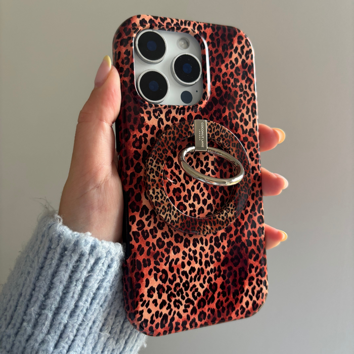 Hand holding a phone with a leopard print case and Coconut Lane MAGSAFE® Phone Ring in leopard pattern against plain background.