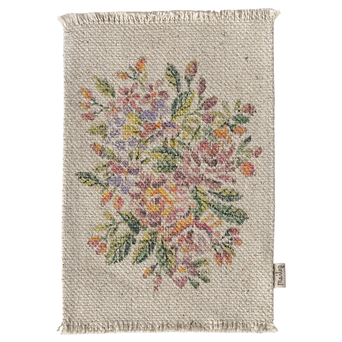 A small rectangular rug with a floral pattern in the center, predominantly featuring pink, yellow, and green colors.