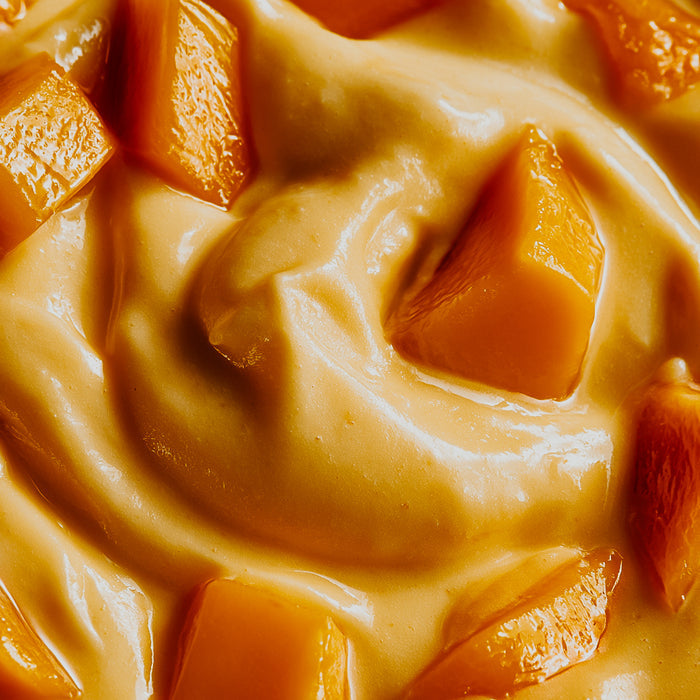 Close-up of a creamy peach-colored dessert or spread with glossy chunks of orange fruit, likely mango or peach, filling the frame.