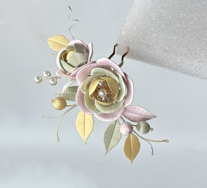 Close up of a pink and sage green silk-wrapped flower hairpin, showing detailed petal layering and pearl stamens.