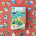 A puzzle box with a colorful illustration of fairy tale characters in a village setting, surrounded by puzzle pieces with various illustrations in the background.