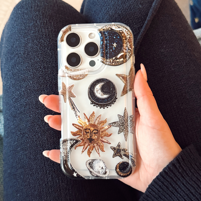 Clear Coconut Lane phone case with sun, moon, star, and planet designs held in a hand.