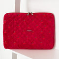 Bright red quilted velvet laptop sleeve with cherry pattern, displayed on a white shelf.
