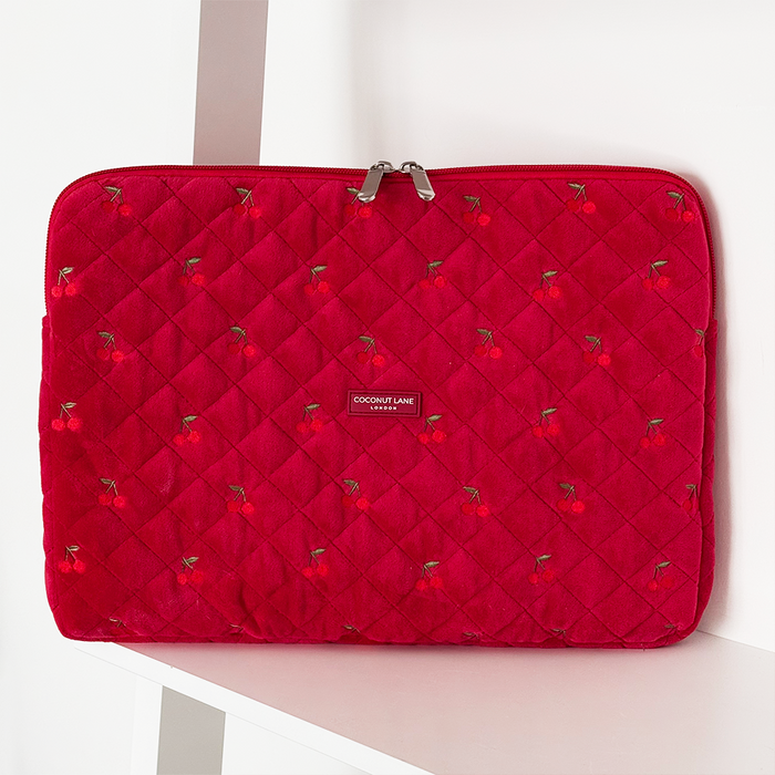 Bright red quilted velvet laptop sleeve with cherry pattern, displayed on a white shelf.