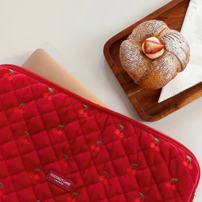 Quilted cherry velvet laptop sleeve next to a croissant on a wooden tray with a napkin.