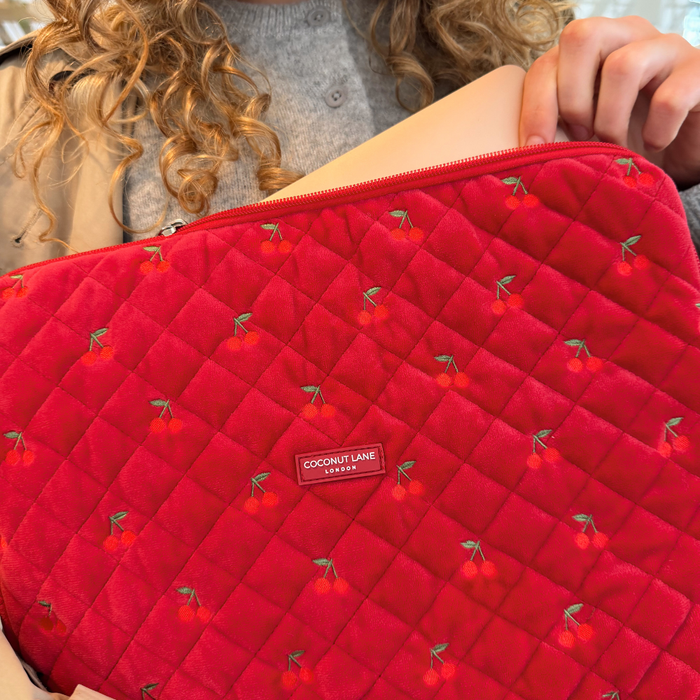 Person holding a cherry red quilted velvet laptop sleeve, wearing a grey sweater.