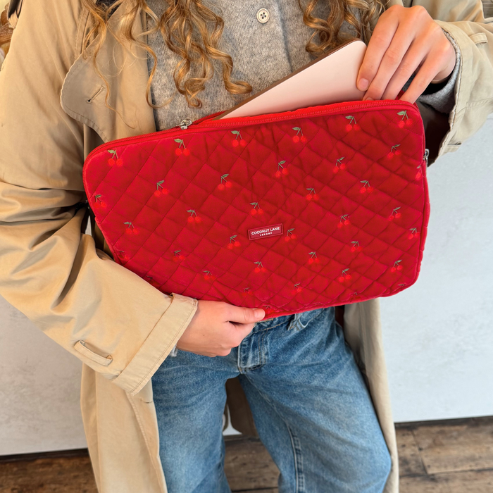 Quilted cherry red velvet laptop sleeve from Coconut Lane held with a visible silver MacBook, person in beige coat.