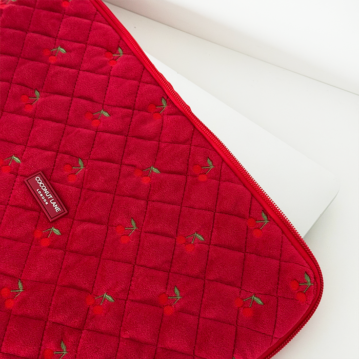 Cherry red quilted velvet laptop sleeve with embroidered cherries, partially covering a laptop.