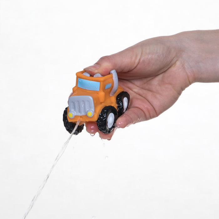 A hand squeezes an orange Nuby Squirt Wheels Bath Squirters truck from the 4 pack, making water squirt from its front. The vibrant bath toy is shown against a plain white background, perfect for imaginative play.