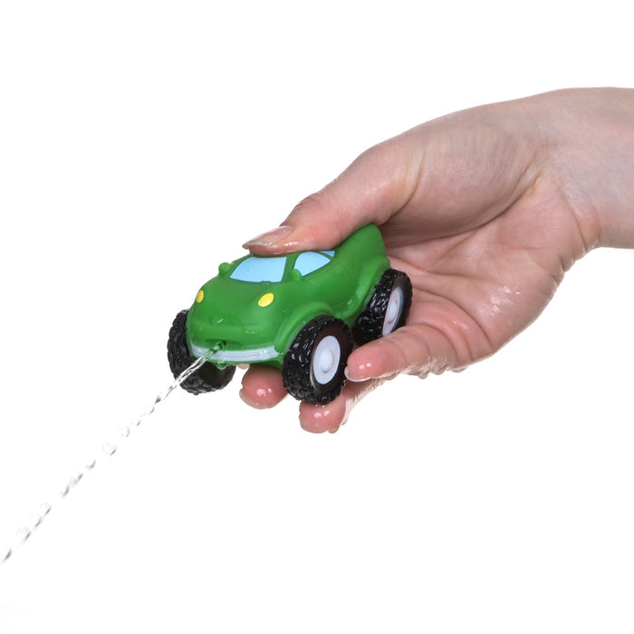 A hand squeezes a green Nuby Squirt Wheels Bath Squirters toy from the 4 pack, making water squirt out from the front—perfect for imaginative play against a white background.