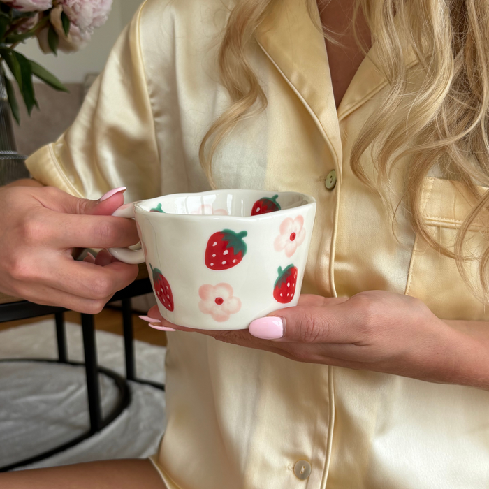 Woman in yellow satin pajamas holding a white mug with strawberry and flower design.