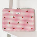 Pink gingham laptop sleeve with small strawberry pattern, displayed on a white shelf.