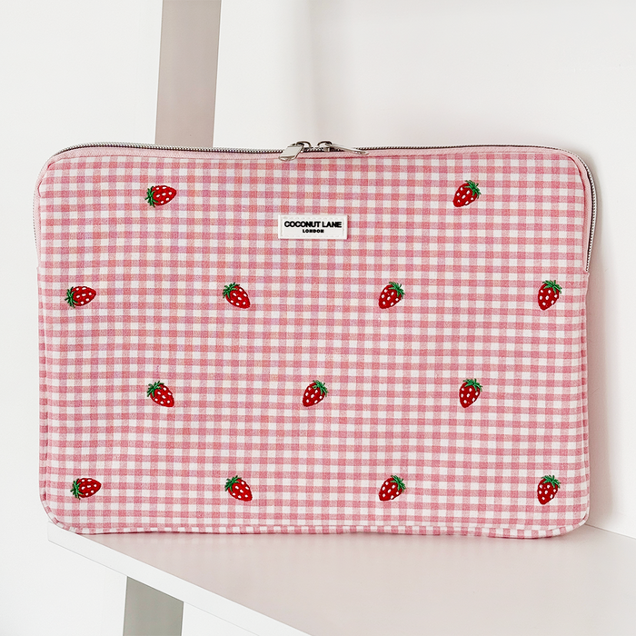 Pink gingham laptop sleeve with small strawberry pattern, displayed on a white shelf.