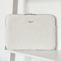 White sherpa laptop sleeve with zipper displayed on a white shelf.
