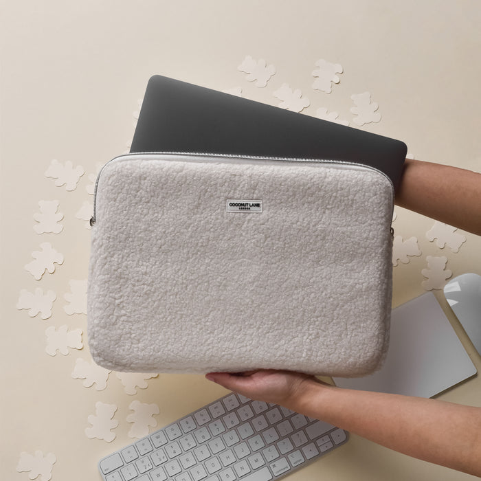 Hand holding a beige Teddy Dolly laptop sleeve above a keyboard with bear-shaped cutouts nearby.