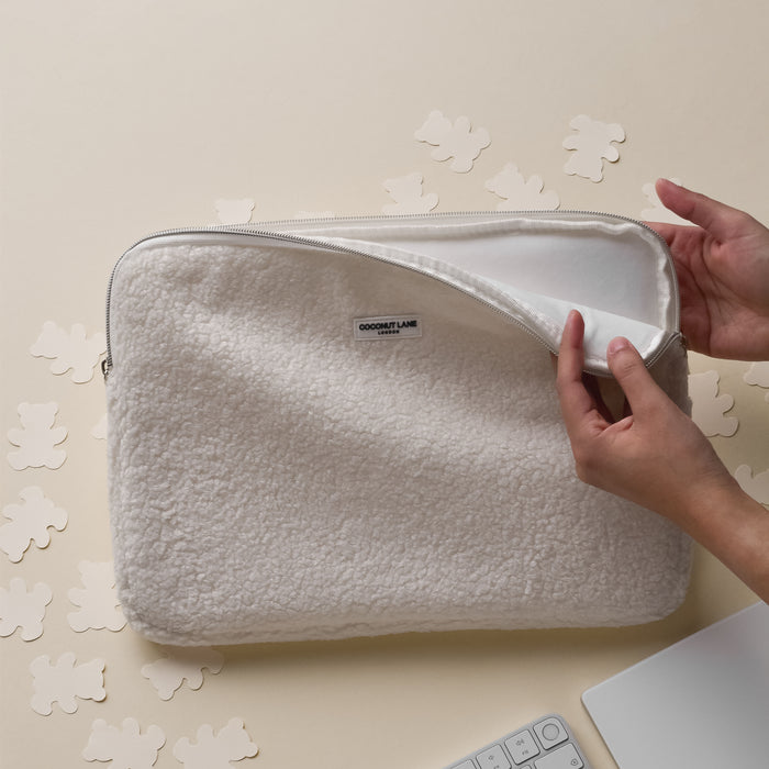 Hands open a beige laptop sleeve with bear cutouts by Coconut Lane on a desk next to a white keyboard.